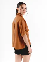 Camisa de manga corta color amarillo claro, con calce oversized, hombros caídos y cierre frontal con botones. Cuenta con bolsillos delanteros con bordados geométricos y mangas con dobladillo.