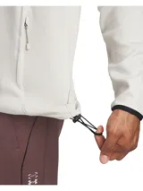 Buzo deportivo de media cremallera Under Armour, color beige claro, con capucha, bolsillos laterales con cierre y puños elásticos. Confeccionado en tejido técnico elástico de alto rendimiento.
