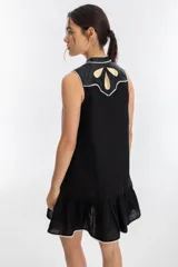 Vestido corto negro de lino con cuello mao y escote en V. Presenta apliques metálicos dorados en los hombros y ruedo con volantes.
