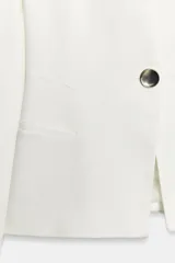Blazer color marfil, entallada en la cintura, con cuello sin solapa, manga larga con hombreras, bolsillos delanteros con solapa y cierre frontal de un botón.