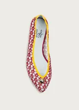 Bailarina de diseño artesanal confeccionada en rejilla bordada con patrón floral en tonos rojizos sobre fondo claro. Presenta ribetes y talón en color amarillo vibrante, con un detalle de media esfera metálica dorada en la puntera y suela plana.