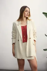 Blazer de lino color beige claro, de corte oversize y doble botonadura con botones marrones. Se combina con un top rojo y una minifalda a juego.