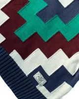 Sweater de cuello alto tejido con diseño geométrico en zigzag multicolor, incluyendo tonos azul marino, verde, bordó y crema. Presenta puños y ruedo acanalados.