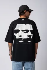 Remera blanca de corte oversize con cuello redondo y mangas cortas. Presenta un pequeño estampado tipográfico en la parte inferior frontal y un diseño gráfico de mayor tamaño en la espalda.