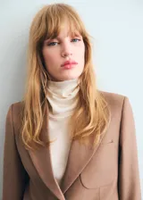 Chaqueta de traje color tostado con cuello de solapa, cierre frontal de dos botones, mangas largas y bolsillos de parche delanteros. Cuenta con forro interior y diseño recto.