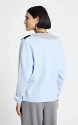 Sweater de punto color celeste con escote en V profundo, ribete acanalado gris y aplicación de encaje negro que delinea el escote. Presenta mangas largas con puños acanalados y dobladillo acanalado.