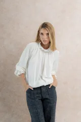 Blusa color crema de tela tejida 100% lana, con cuello fruncido y mangas largas con puños elásticos.