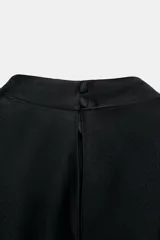 Vestido midi de satén negro con cuello subido, manga corta tipo capa y pañuelo incorporado en el mismo tejido. Presenta aberturas laterales decoradas con encaje a tono y bajo asimétrico con detalles de encaje. Cierre en la espalda con abertura y botones forrados.