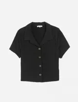 Camisa cropped negra de manga corta, con cuello solapa y cierre frontal de botones.