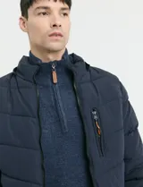 Campera capitoneada de poliéster color negro, con capucha desmontable, cierre frontal y bolsillo en el pecho con cierres engomados y tiradores en color naranja.