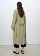 Abrigo largo de diseño recto y fluido, color verde oliva, con cuello de solapa con muesca, cierre delantero y cinturón tipo batín para ajustar a la cintura. Posee mangas largas con trabillas y dos bolsillos laterales.