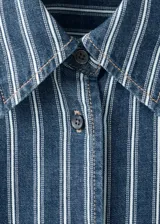 Camisa oversize de algodón estilo denim, de color azul con estampado de rayas, cuello camisero, manga larga con puños abotonados, bolsillo de parche en el pecho y cierre frontal con botones.