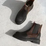 Botas estilo Chelsea de cuero color marrón, con paneles elásticos laterales negros, presillas traseras y suela chunky de goma negra con plataforma dentada.