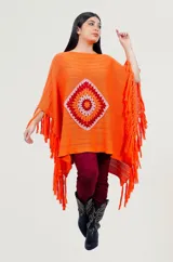 Poncho rojo de tejido artesanal con aplique central de crochet en forma de mandala con tonos amarillos, blancos y rojos. Presenta terminación con flecos en los laterales y diseño holgado.