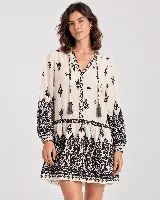 Vestido corto color beige con estampado ornamental en color negro, escote en V con cordones y borlas colgantes, y mangas largas.