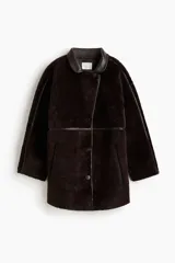 Abrigo de textura afelpada en color marrón oscuro, con cuello, ribetes y detalles en cuero sintético. Presenta un corte holgado, cierre frontal con botones, mangas raglán y bolsillos laterales.