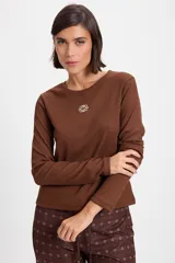 Remera de manga larga con textura acanalada y silueta ajustada. Presenta cuello redondo y un pequeño bordado decorativo en el centro del pecho.