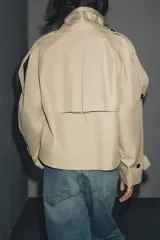 Trench corto negro confeccionado en hilatura con mezcla de algodón. Cuello solapa de muescas ajustable con trabilla y botones. Manga larga. Bolsillos delanteros. Detalle de trabillas en hombros. Cierre frontal cruzado con botones.