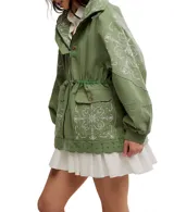 Chaqueta estilo parka o anorak de algodón color verde militar, con capucha y cordón ajustable en la cintura. Presenta parches de tela con bordados blancos de estilo paisley o floral en la parte delantera, mangas y capucha. El ruedo inferior tiene un borde festoneado con ojales.