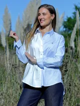 Camisa de corte holgado confeccionada en algodón, con diseño bicolor que combina blanco y celeste. Presenta cuello clásico, cierre frontal con botones, mangas largas con puños abotonados y dobladillo redondeado.