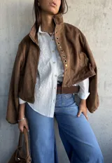 Camisa blanca de corte clásico con sutiles rayas verticales y delicado bordado floral en la parte superior delantera. Presenta cuello camisero, cierre frontal con botones y mangas largas.