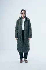 Campera acolchada de largo midi en color verde militar, con diseño de matelassé, cierre frontal con botones y cuello camisero. Presenta un corte relajado y bolsillos laterales.