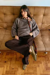 Jersey de punto color marrón topo, con cuello drapeado decorado con un broche metálico dorado y mangas largas de corte holgado.