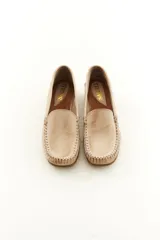 Mocasines de cuero vacuno color beige con acabado mate, costuras visibles artesanales en el empeine y suela de perfil bajo.