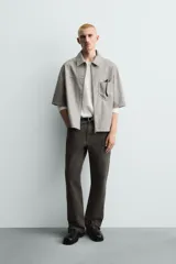 Sobrecamisa de corte relajado confeccionada en tejido efecto piel, con cuello solapa, manga corta, bolsillo plastrón en el pecho y cierre frontal con cremallera.