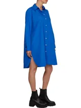 Vestido camisero de corte oversize confeccionado en algodón orgánico. Presenta cuello inglés, cierre frontal de botones, mangas largas con puños abotonados y largo hasta la rodilla. Incluye el logo de la marca bordado en uno de los puños.