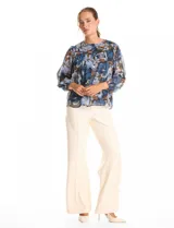 Blusa de gasa con estampado floral en tonos azules y marrones, con sutiles hilos de lurex dorados. Presenta cuello a la base, abertura central con botones, canesú delantero con pasamanería calada y mangas largas con puños elastizados. Incluye forro interno a tono.