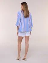 Blusa Erika de algodón con estampado de rayas en tonos azules, rosados y amarillos. Presenta cuello redondo con escote en V y botones frontales, mangas cortas decoradas con una fila de botones en los laterales y dobladillo asimétrico.