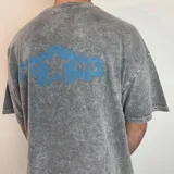 Remera de corte boxy con efecto lavado ácido en color gris. Presenta un estampado gráfico en la espalda con una franja azul horizontal, una estrella central y la inscripción 'WHITE NOISE'.