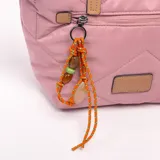 Bandolera rosada acolchada con diseño geométrico pespunteado, asas de mano en color tostado y correa ajustable desmontable. Cuenta con un bolsillo frontal con cierre y un llavero colgante de cordón naranja con cuentas decorativas.