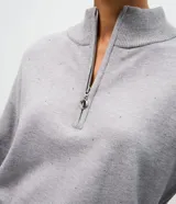 Suéter de punto color gris con cuello alto y medio cierre frontal. Presenta mangas largas con puños ajustados y una sutil aplicación de brillos en la parte frontal.