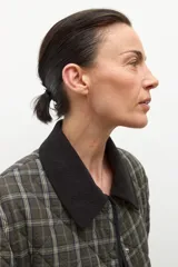 Campera capitoneada de corte recto con diseño a cuadros en tonos verde oliva y gris. Presenta cuello camisero de pana en color negro, cierre frontal con botones a presión y bolsillos laterales amplios con ribete negro.