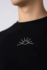 Remera de corte oversize confeccionada en algodón pesado con textura de micropanal. Presenta un diseño minimalista con un pequeño bordado lineal de un sol en el centro del pecho.