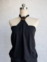 Vestido corto negro con escote halter y detalle de argolla decorativa en el cuello. Presenta un diseño drapeado en la parte superior y falda ajustada.