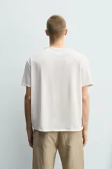 Camiseta de corte relajado con cuello redondo amplio tipo panadero, con detalle de botones y acabado irregular. Manga corta.