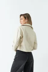 Campera de cuero sintético en color crema, con diseño ajustado al cuerpo y largo hasta la cintura. Presenta cierre frontal con botones, bolsillos con solapa y detalles de cierres metálicos en los puños.