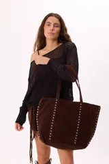 Bolso tipo tote de gamuza sintética en color marrón, con diseño amplio y manijas largas. Presenta dos líneas verticales de tachas metálicas plateadas en el frente y en los laterales.