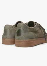 Championes urbanos Satorisan modelo Heisei, confeccionados en gamuza color verde oliva con suela de goma color marrón. Presentan cordones al tono y detalles metálicos en los ojales.