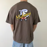 Remera marrón de corte boxy, manga corta y cuello redondo. Presenta un gran estampado en la espalda de un tiburón caricaturizado con bermudas rojas y la inscripción "Midway" en color amarillo.