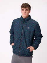 Campera reversible de nylon con cierre frontal, cuello alto y bolsillos laterales. Presenta un estampado geométrico en tonos oscuros y turquesa.