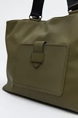 Bolso negro tipo shopper de símil cuero con terminación suave. Tiene asas anchas de cinta y un bolsillo frontal con solapa.