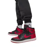Pantalon de jogging Nike Jordan, confeccionado en tejido fleece color negro, con cintura elástica ajustable mediante cordón, puños elásticos en los tobillos y logo Jumpman bordado en color rojo en la pierna izquierda.