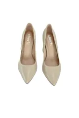 Stilettos de cuero color trigo con punta fina y tacón geométrico que combina madera clara con detalles dorados.