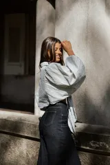 Camisa de algodón con diseño a rayas verticales en tonos blanco y gris. Presenta un corte oversize con mangas abullonadas y un nudo frontal que permite ajustar la prenda a la cintura.