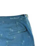 Short de baño color azul petróleo con estampado sutil de palmeras. Presenta una pretina fija con hebillas metálicas laterales para ajuste, cierre frontal con botón a presión, dos bolsillos laterales y un bolsillo trasero. Incluye interior con mesh hipoalergénico.