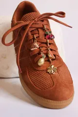 Zapatillas bajas color marrón con cordones y charms dorados.
